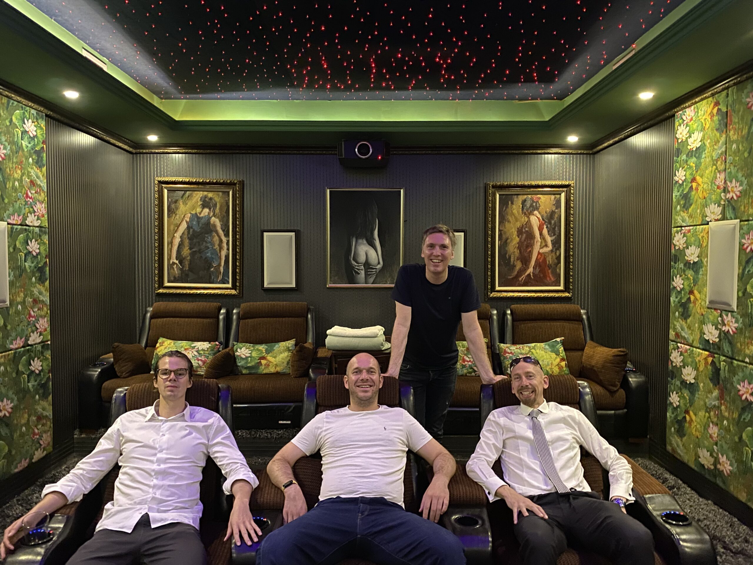 Four men in a luxury room with brown recliners and floral panels