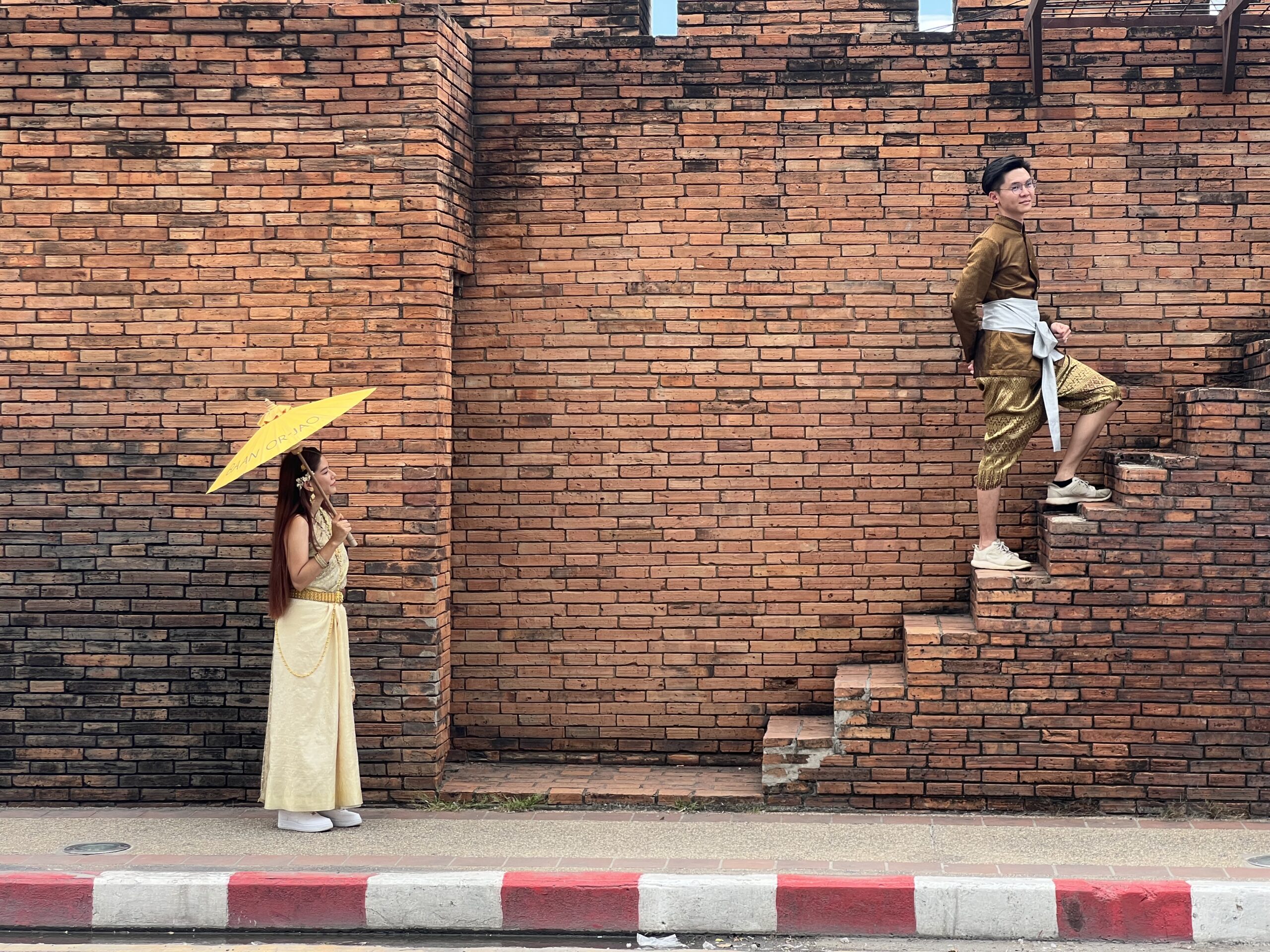 Woman and man in traditional Thai attire on ancient brick wall steps