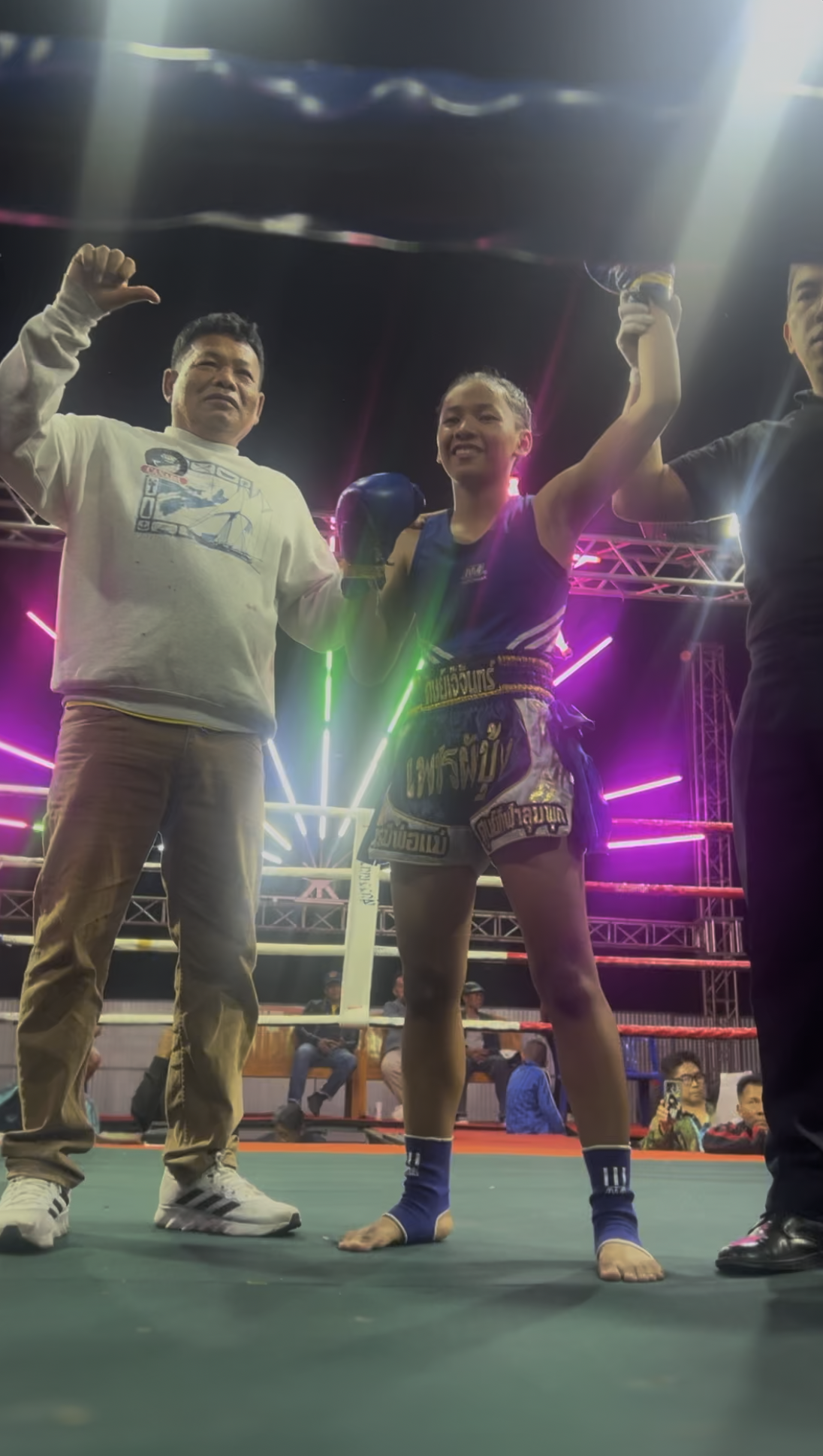 Victorious Thai female Muay Thai fighter in victory pose with trainer